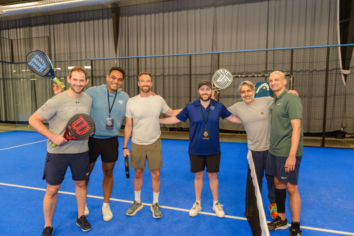 Six across the blue padel court, paddles in hand